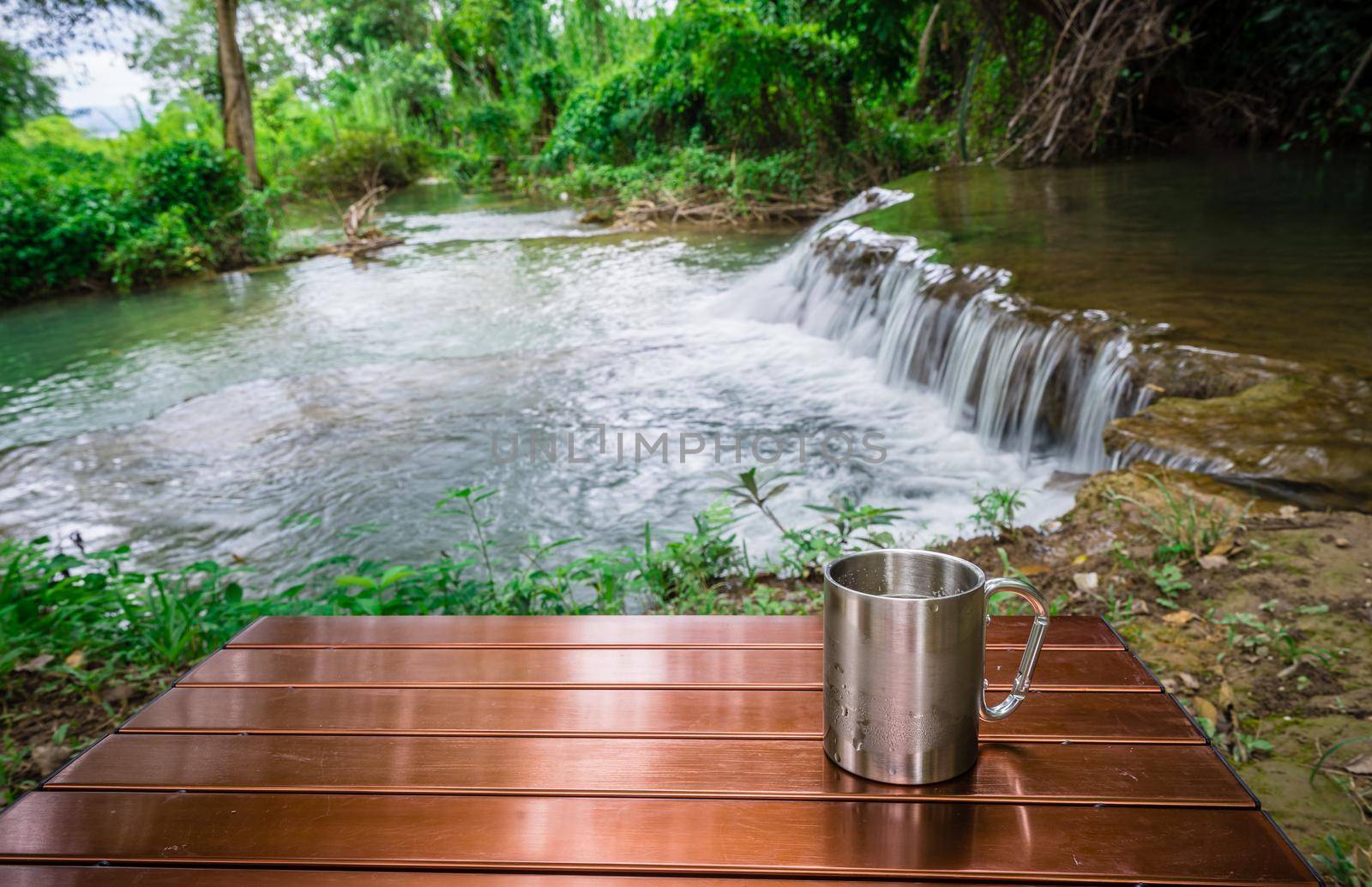 cup of cold drink on the table in front of the waterfall between camping on holiday by domonite