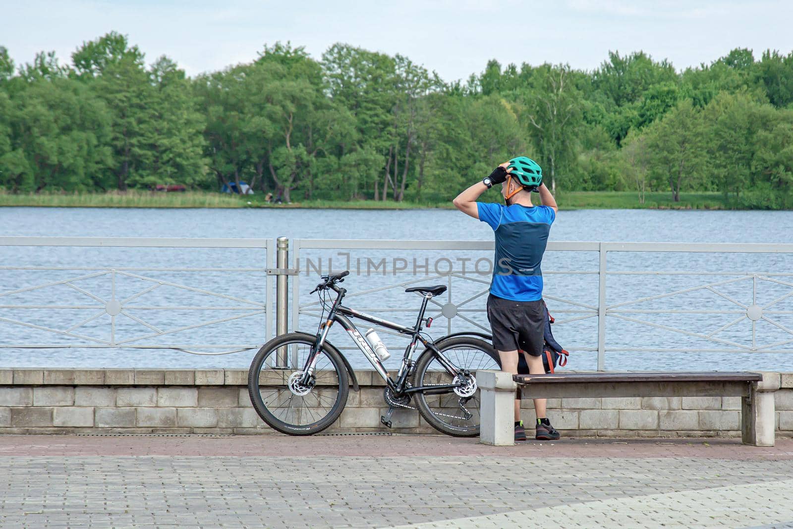 Belarus, Minsk - May 28, 2021: Male cyclist resting on the embankment of the reservoir and looks into the distance at the water. Stock photography.
