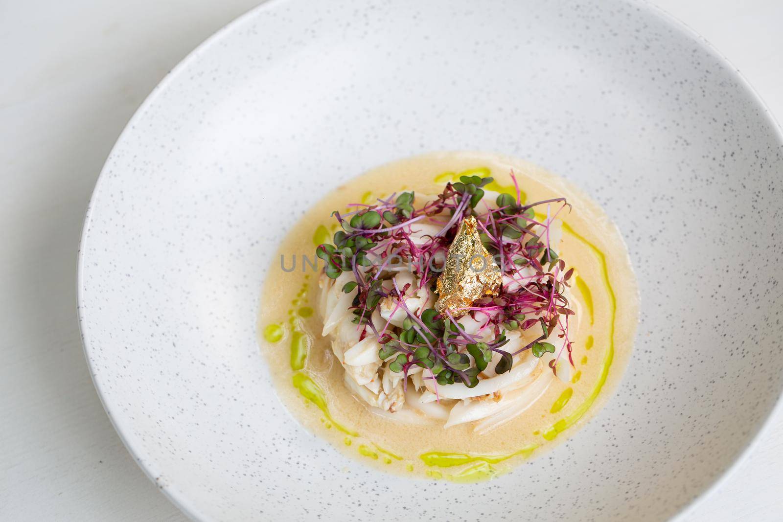 Crab meat in coconut cream soup and micro greens over gray concrete background. Top view, copy space. Healthy delicious breakfast.