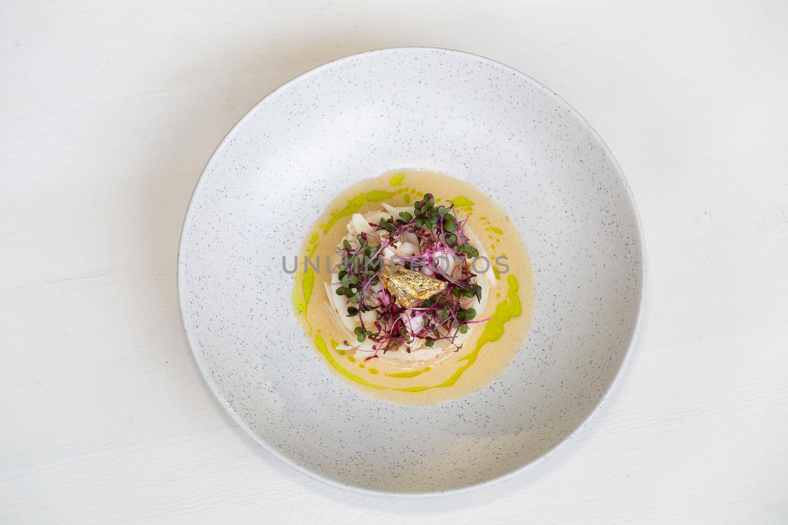 Crab meat in coconut cream soup and micro greens over gray concrete background. Top view, copy space. Healthy delicious breakfast.