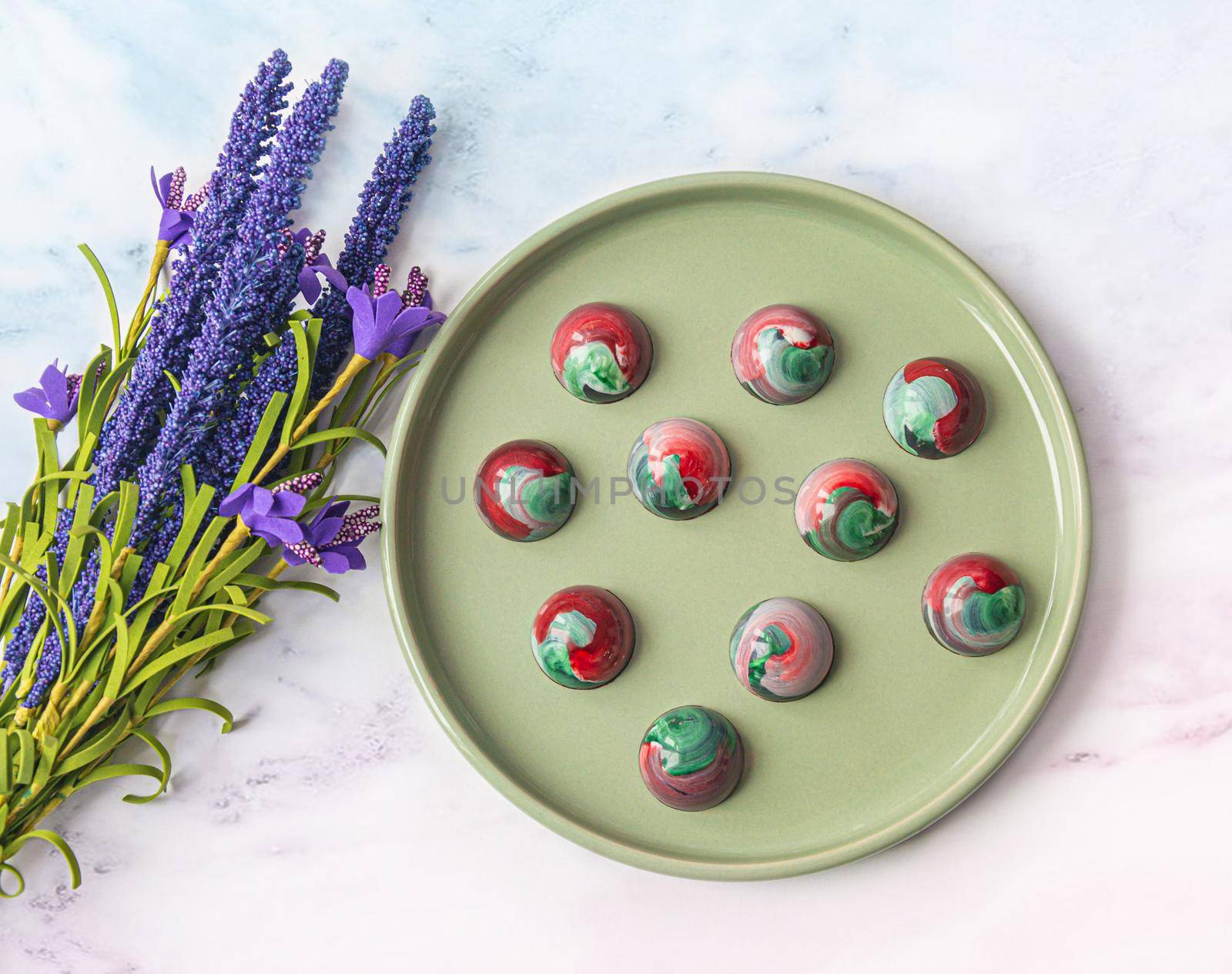 Collectible handmade tempered chocolate sweets with a glossy painted body on a round plate with blur elements. View from above. Stock photography.