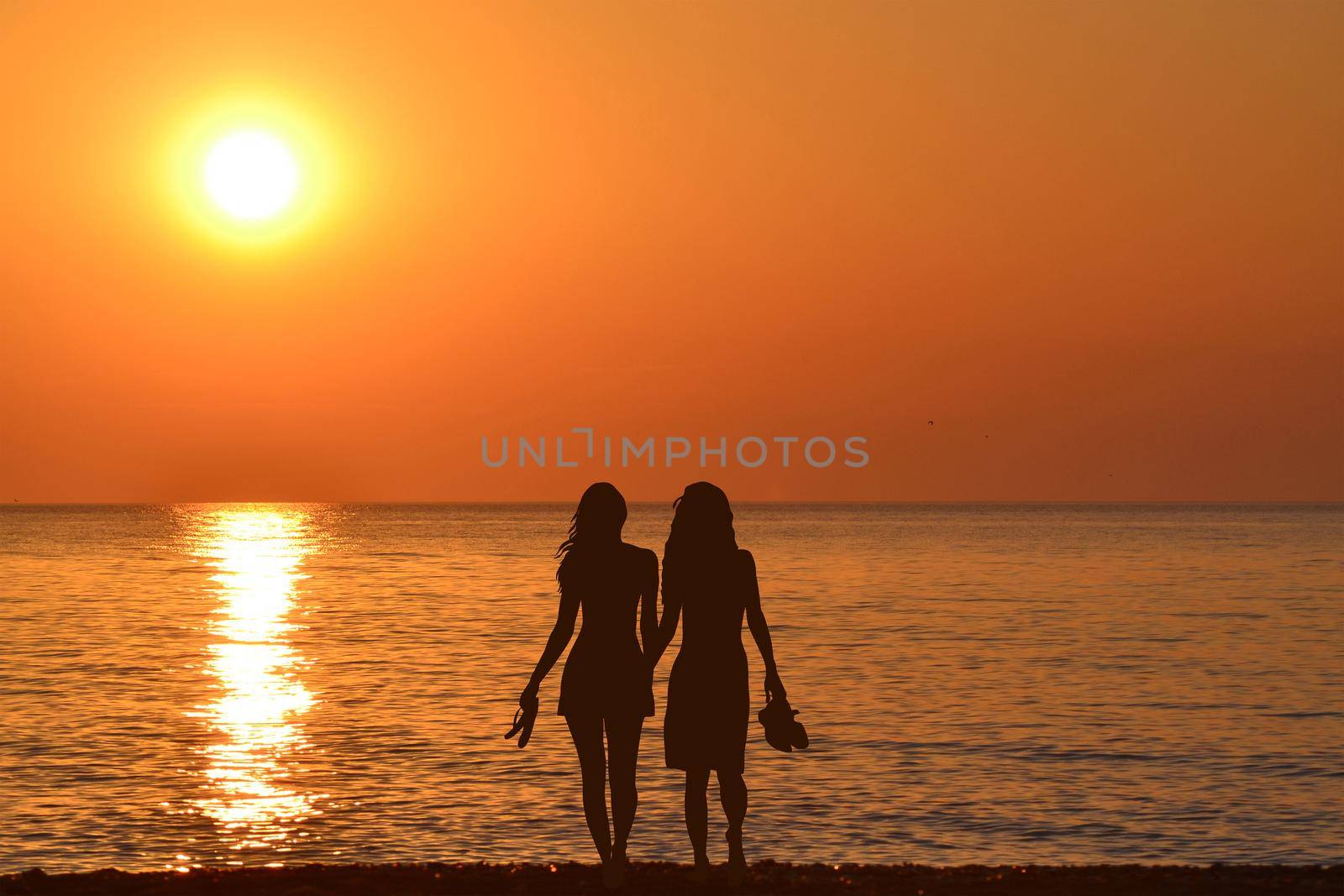 Two young women holding hands walking barefoot with slippers in his hand on the beach by hibrida13