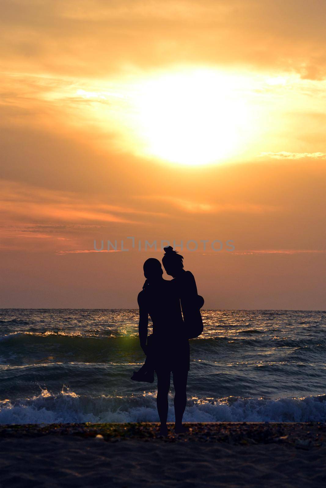 Silhouette of man carrying woman in his arms on the beach at sunset