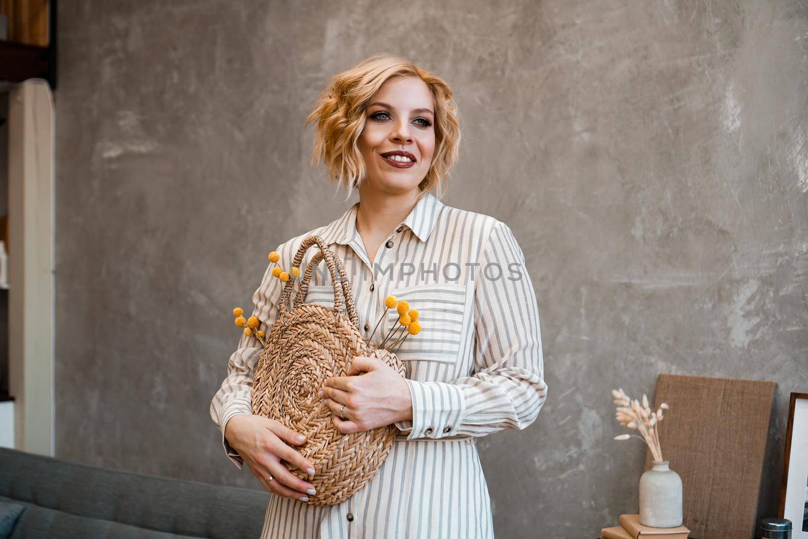 Young beautiful stylish woman at home wearing dress, safari style, straw bag