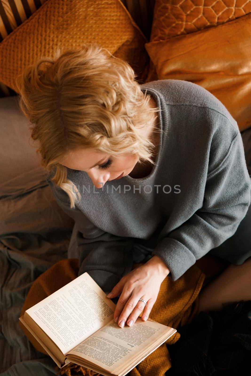 Blonde woman reading book on bed - cozy room