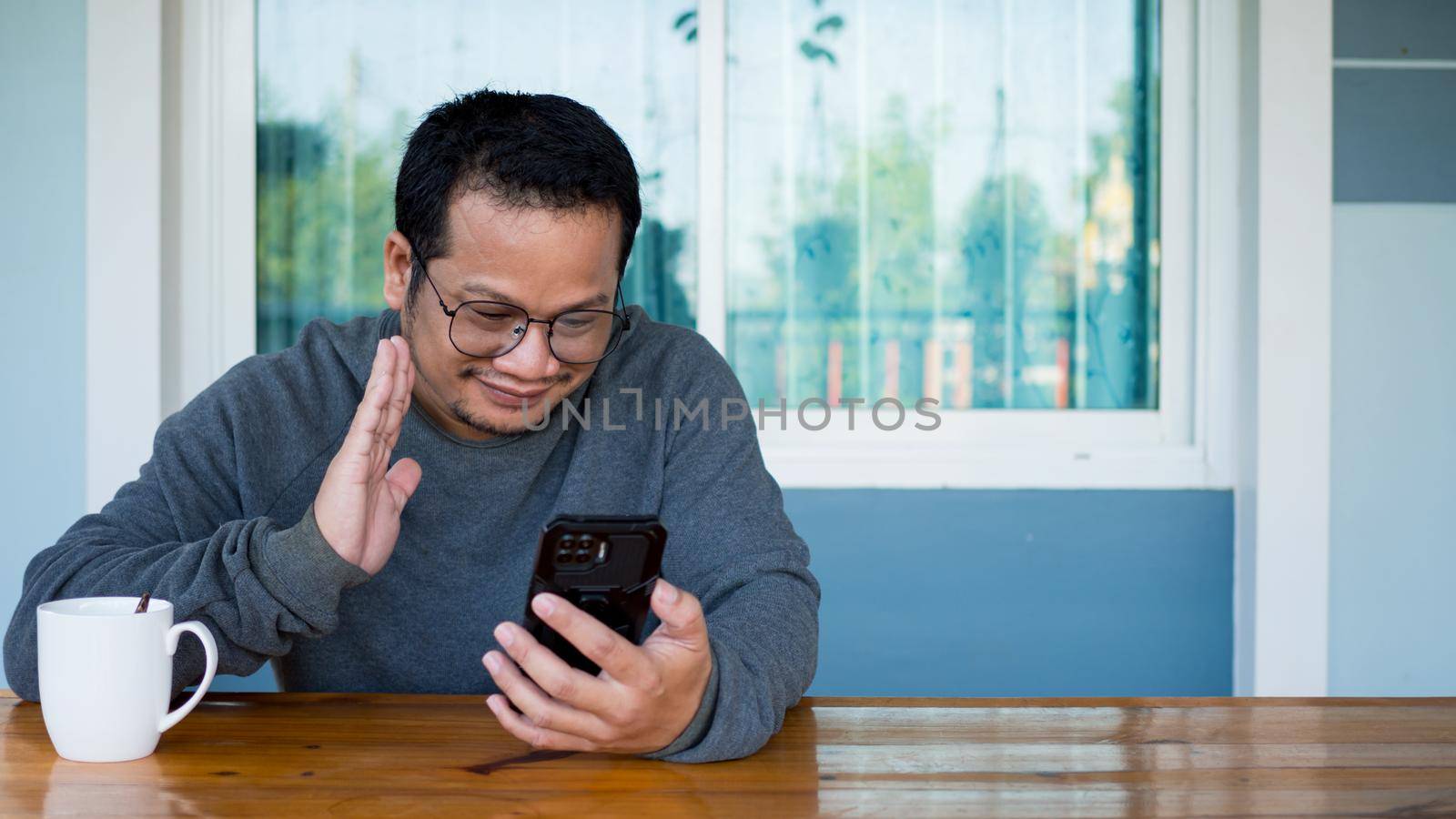 Asian men wearing long sleeves and eyeglasses Sitting and talking on a video chat with a smartphone. communication concept. by Unimages2527