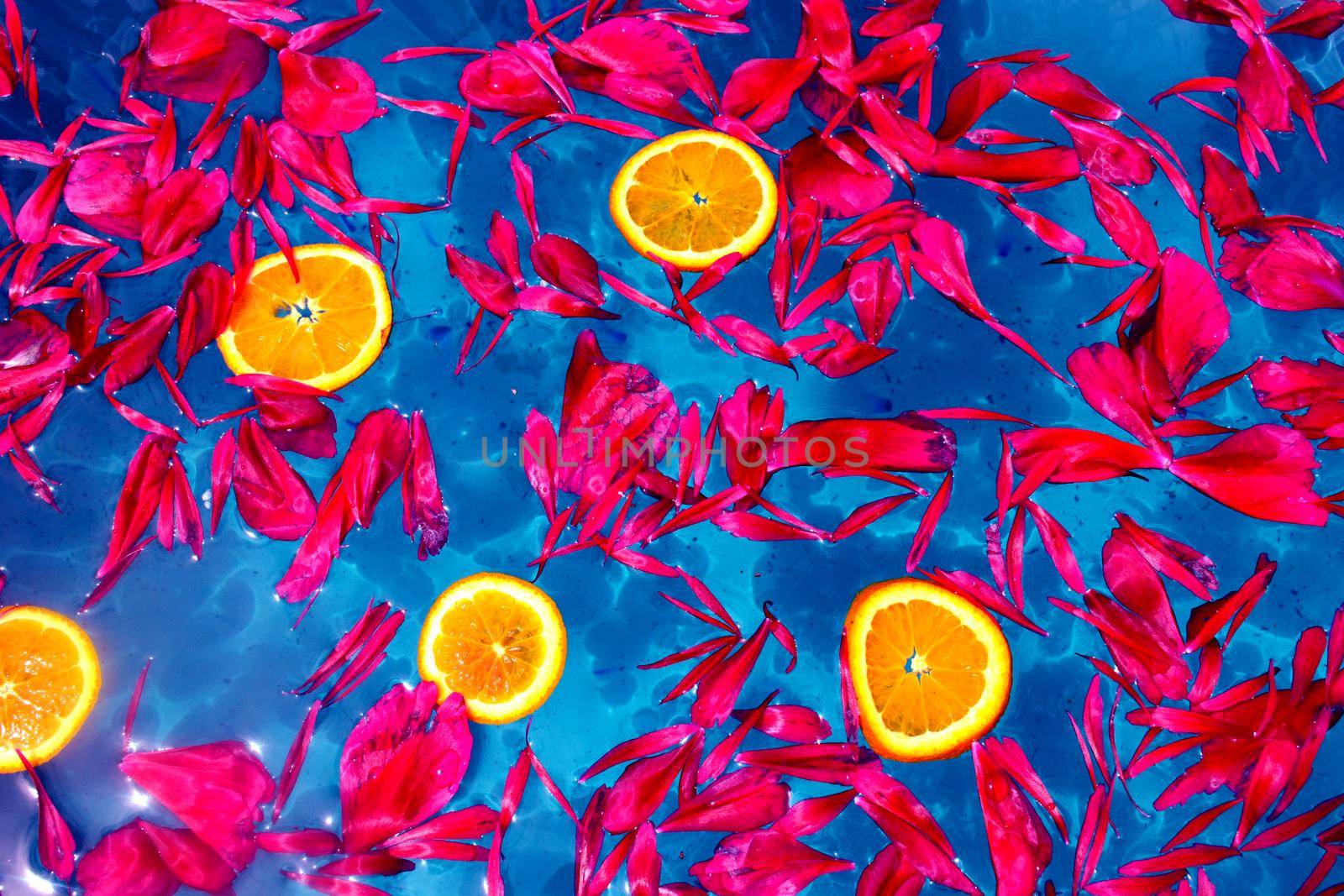 Red petals and orange slices floating on blue water