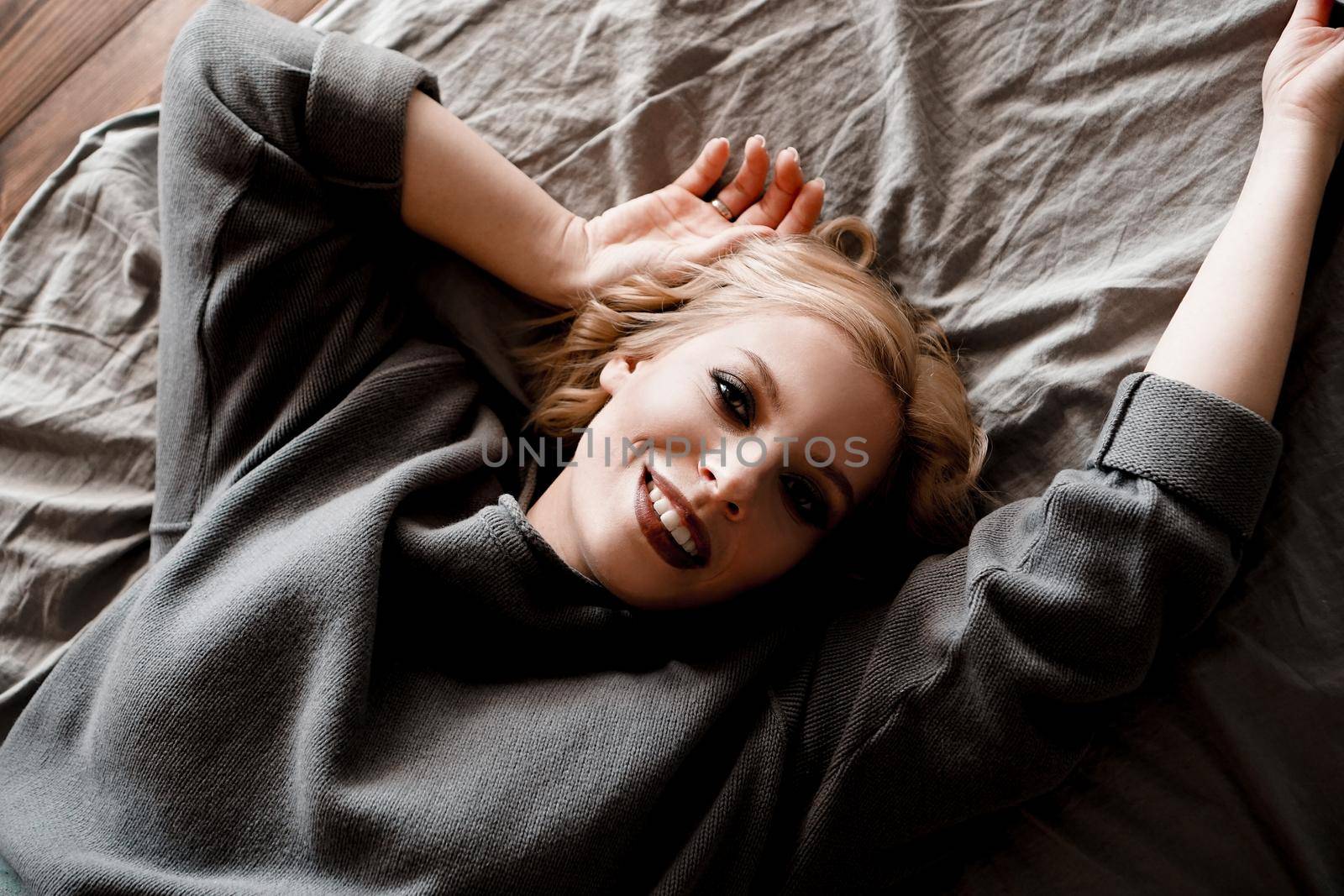 Beautiful young woman in gray sweater laughing lying in bed by natali_brill