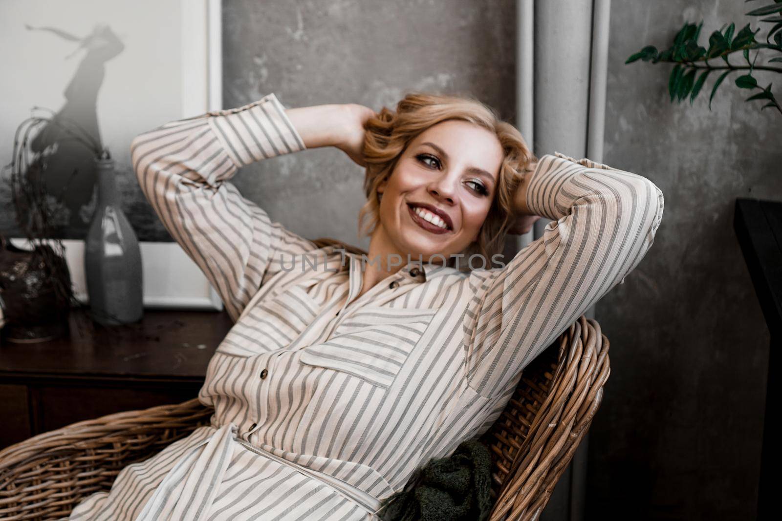 Beautiful young woman resting at home in a wicker chair near the window with plants