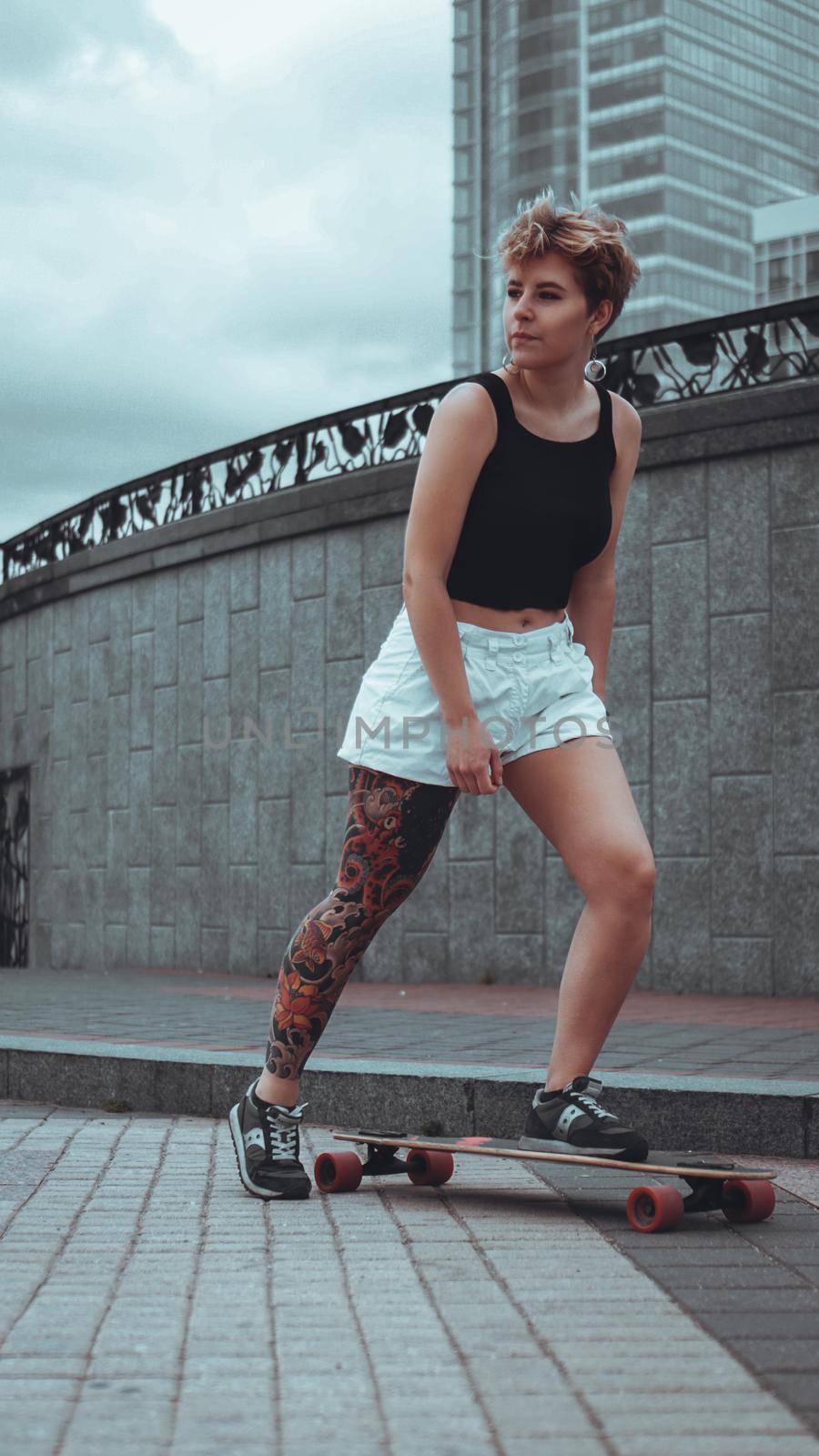 Beautiful young girl with tattoos with longboard in the town. She has traditional japanese tattoo