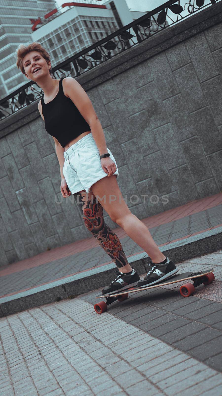 Beautiful young girl with tattoos with longboard in the town. She has traditional japanese tattoo