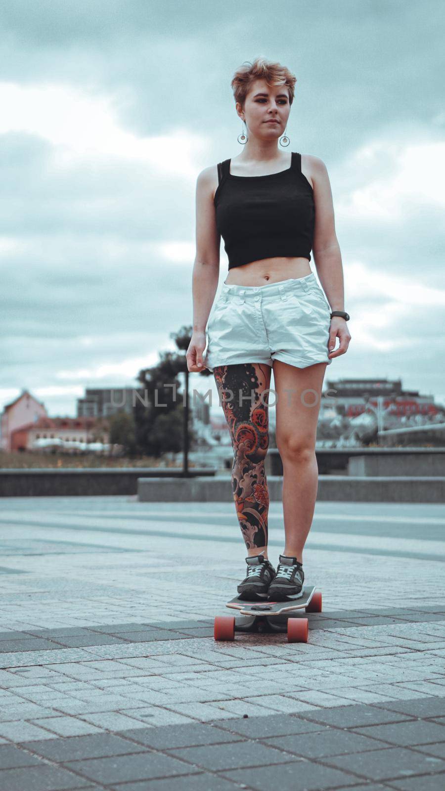 Beautiful young girl with tattoos with longboard in the town. She has traditional japanese tattoo