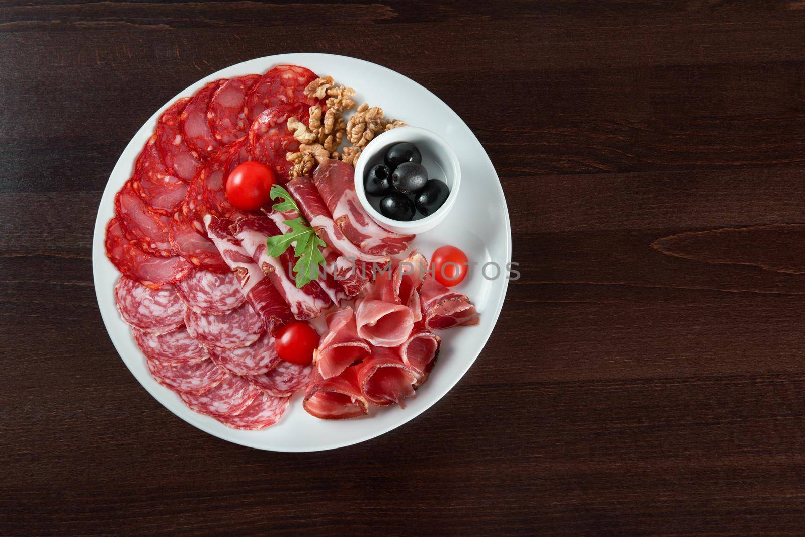 Salami appetizers. Sliced salami and ham of different kinds served on a plate with cherry tomatoes walnuts and black olives food concept top view copyspace