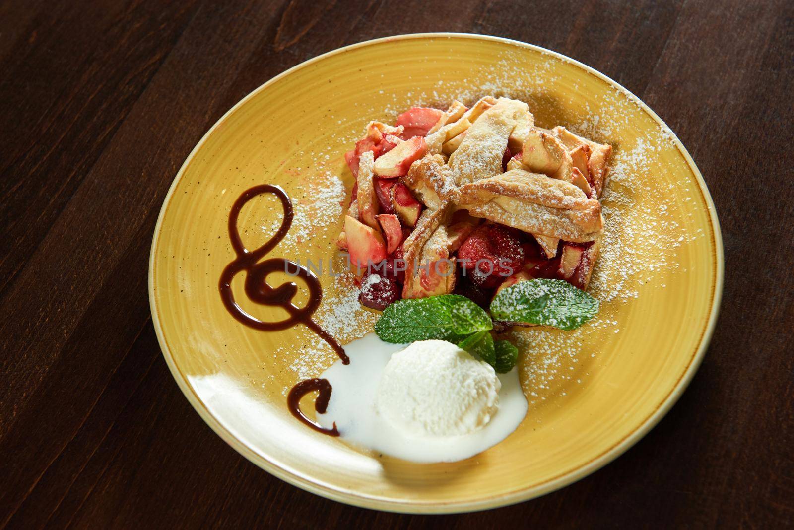 Rich taste. Piece of mouthwatering fruit strudel decorated with mint and served with a scoop of ice cream