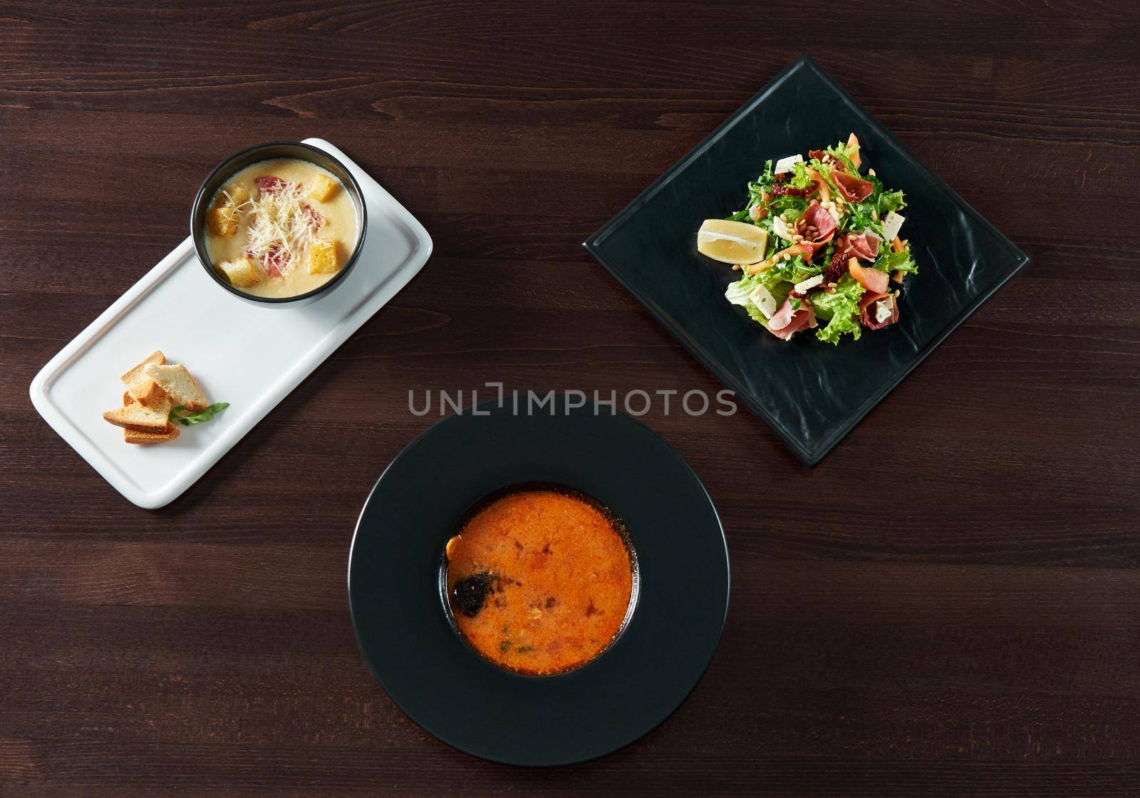 Enjoyment served. Top view of a gazpacho cold Spanish soup served with cheese cream soup with croutons and a plate of salad with arugula and prosciutto