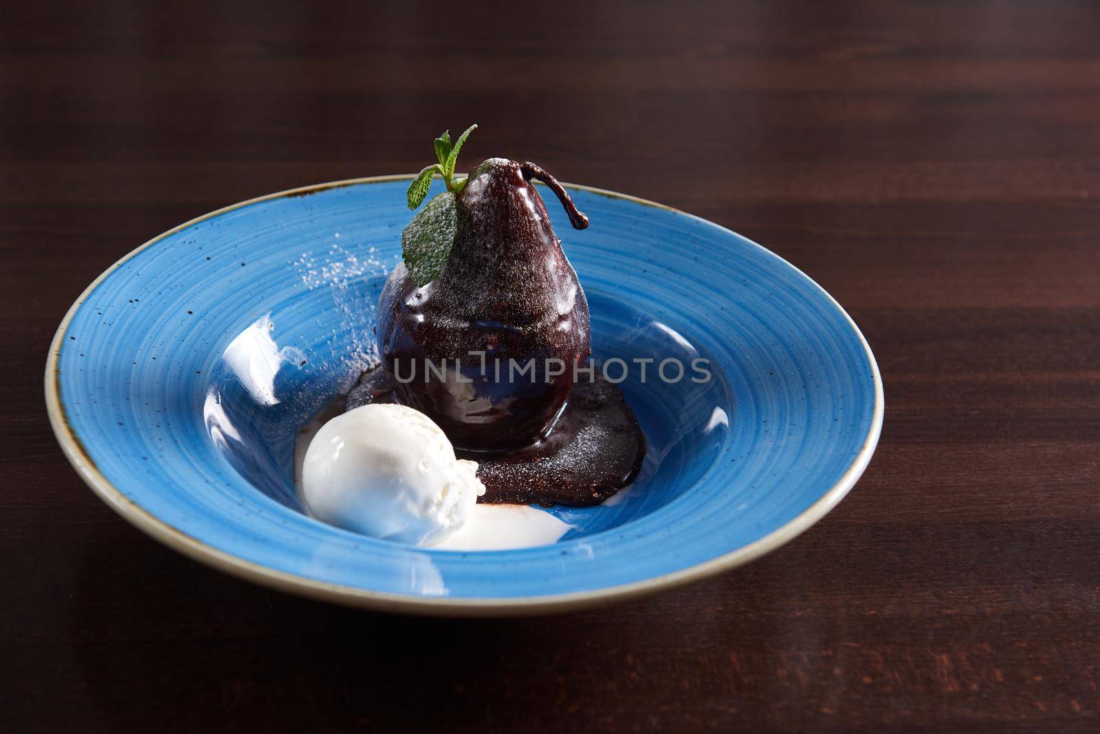 Heavenly sweetness. Closeup of a delicious dessert poached pear covered with chocolate glazing served with a scoop of ice cream in a rustic blue bowl copyspace
