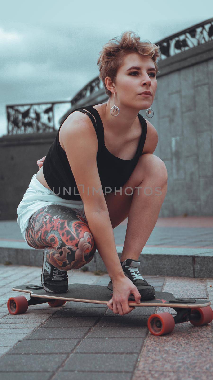 Beautiful young girl with tattoos sits on longboard. She has traditional japanese tattoo