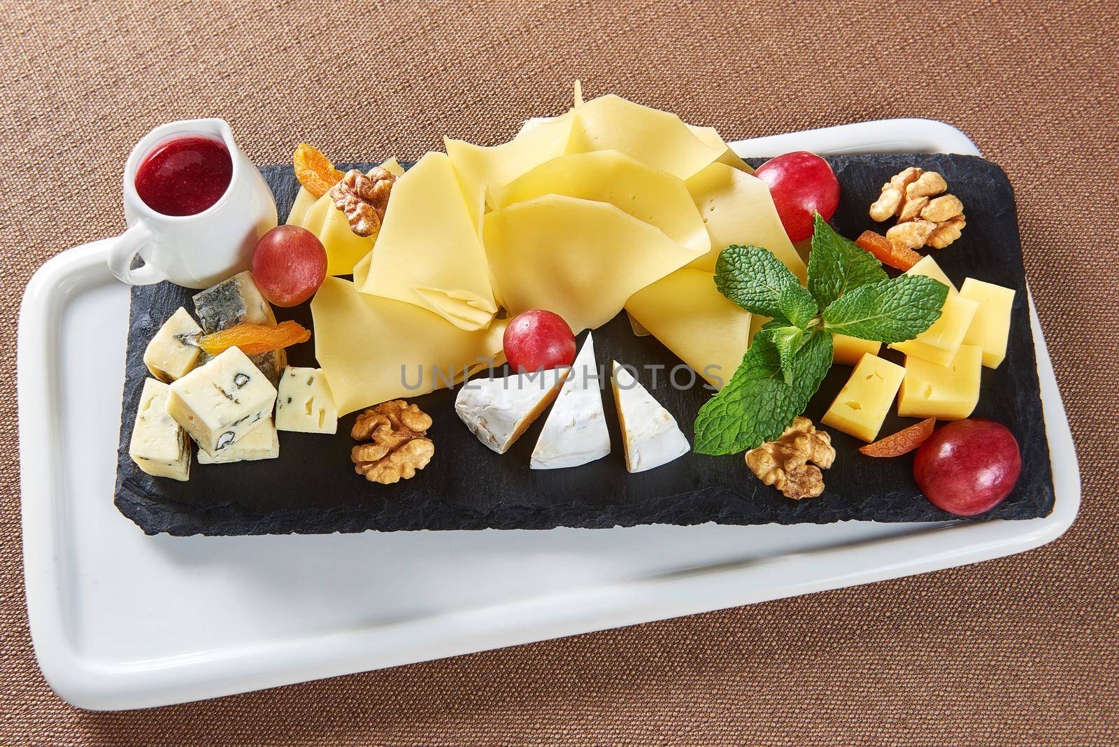Appetizers served. Top view of a cheese plate with Gouda cheese brie blue cheese walnuts grapes and a little jar of jam