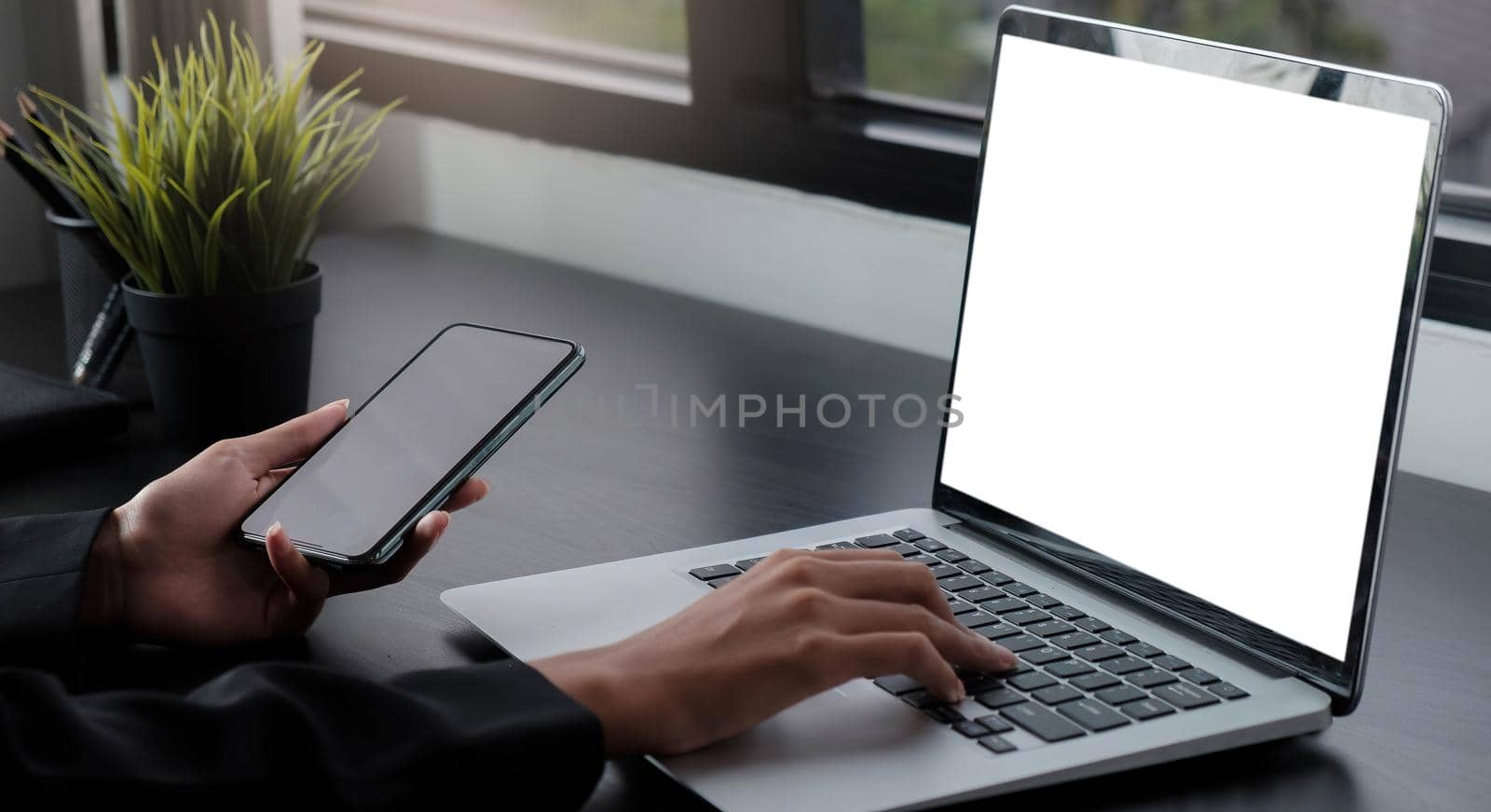 Cropped shot of business woman hand while typing on computer tablet with blank screen and holding smartphone on sitting next to her colleague by wichayada