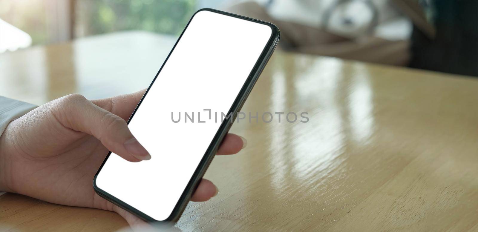 Mockup image blank white screen cell phone.women hand holding texting using mobile on desk at home office. by wichayada