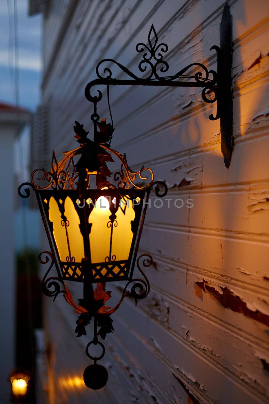 Glowing old street lamp lighting on the facade of the house. Twilight on the street of the old city.