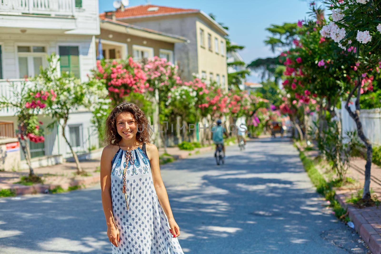 A charming brunette girl walks along the street of Buyukada island in Turkey. Summer sunny day and blossoming trees by Try_my_best