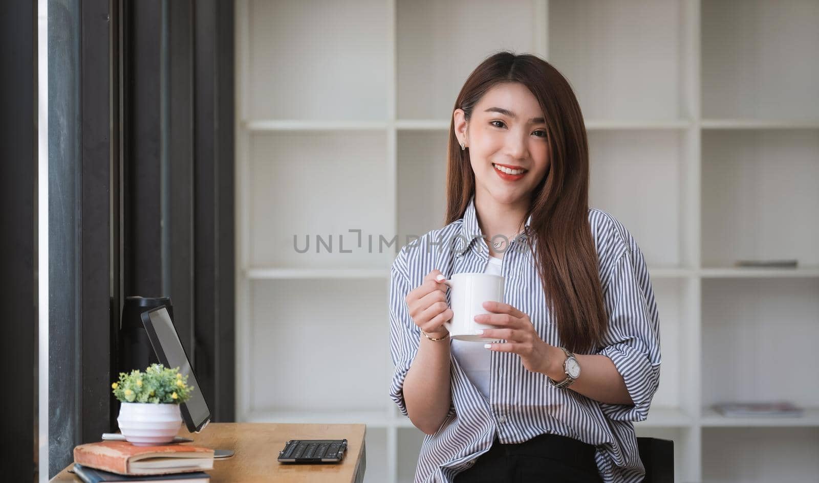 Asian woman drinking coffee and relax in coffee shop cafe. Beautiful female looking at camera during working with digital tablet.