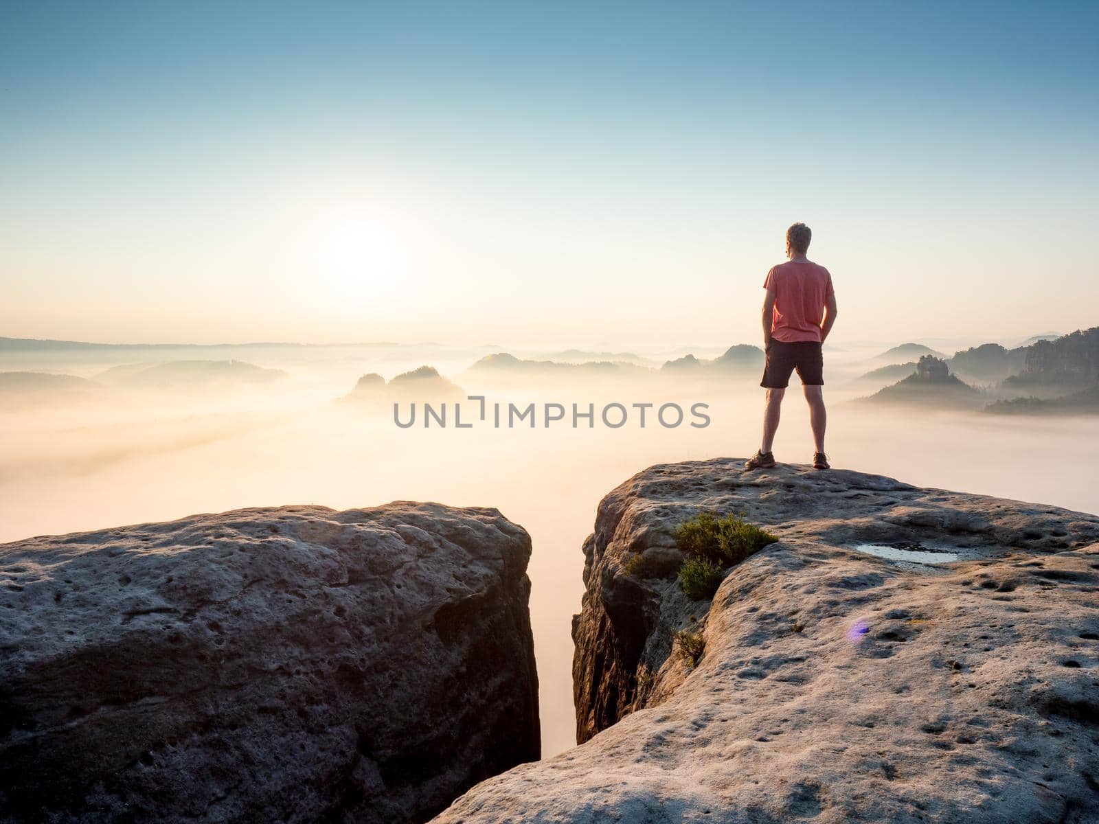 Tourist  or hiker on the peak of high rocks watching morning mist in landscape. Sport and active life concep 