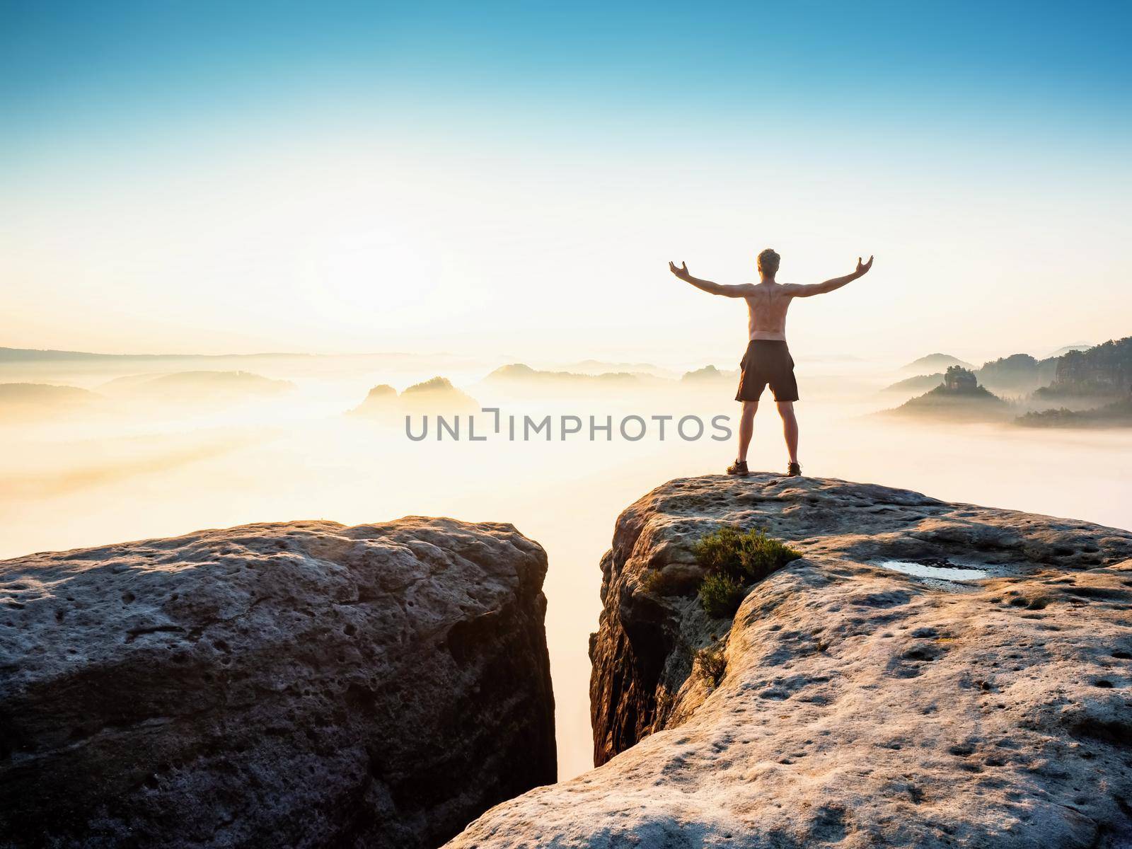 Happy shirtless man standing above a morning  cloudscape with open arms and greeting to sun, world and everything