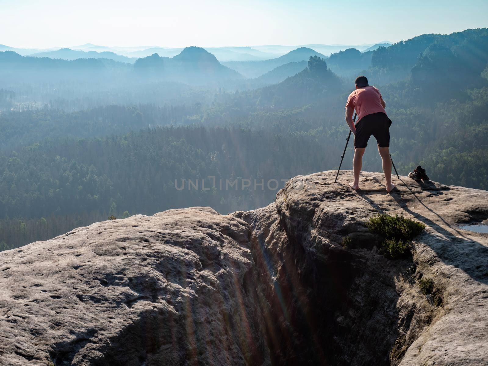 Professional photographer stay barefoot at tripod on mountain summit.  Artist on location and nature photographer photographing landscape outdoor