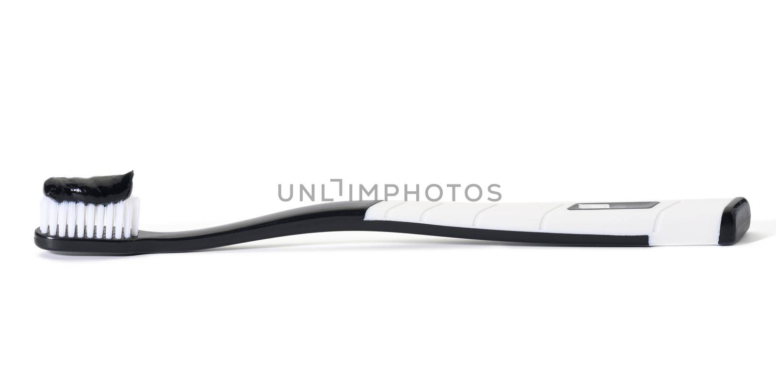 white plastic toothbrush with black charcoal paste on white background by ndanko