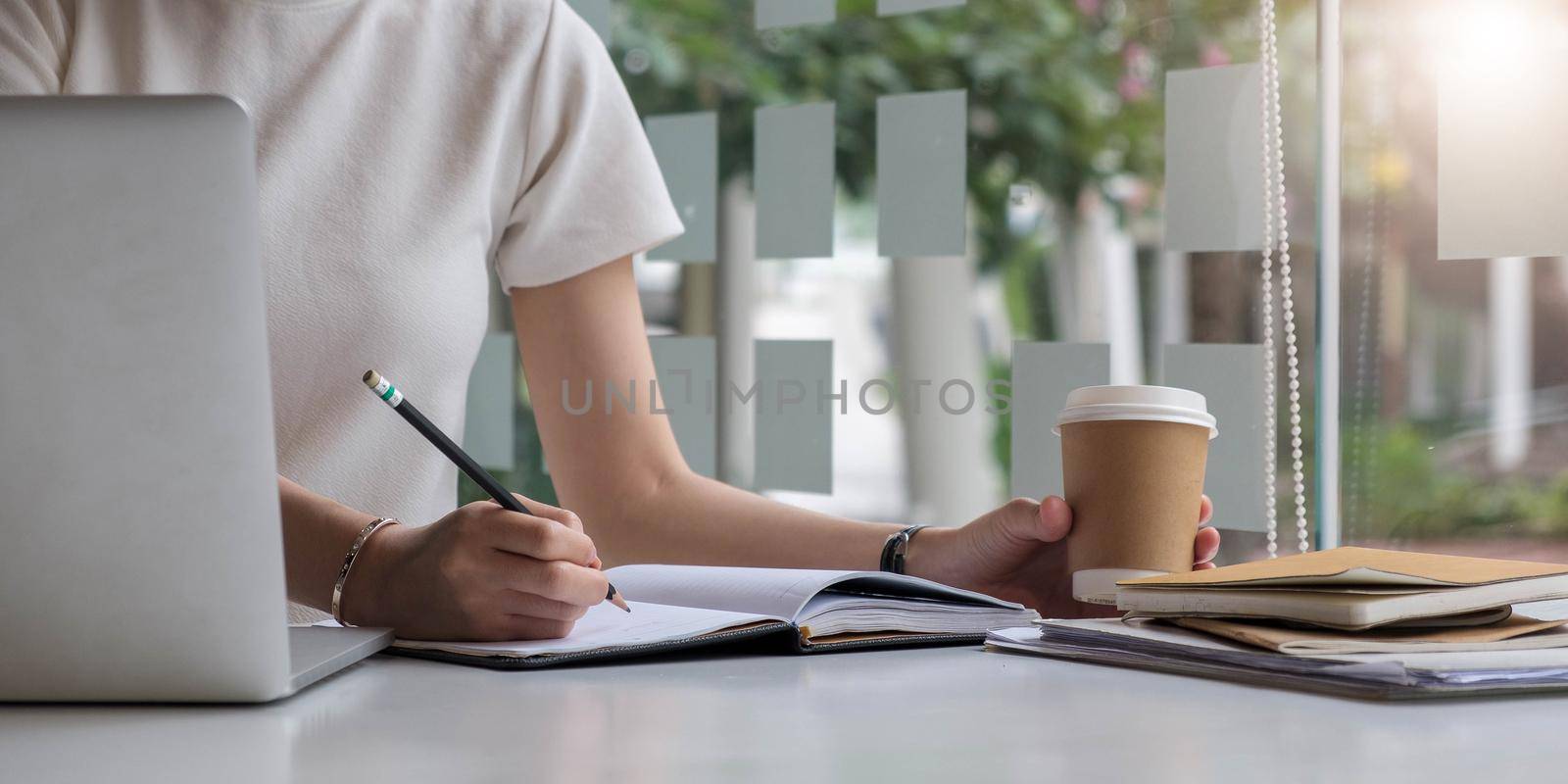 Close up of hand businesswoman writing on paper and using laptop to searching data for working or online learning.