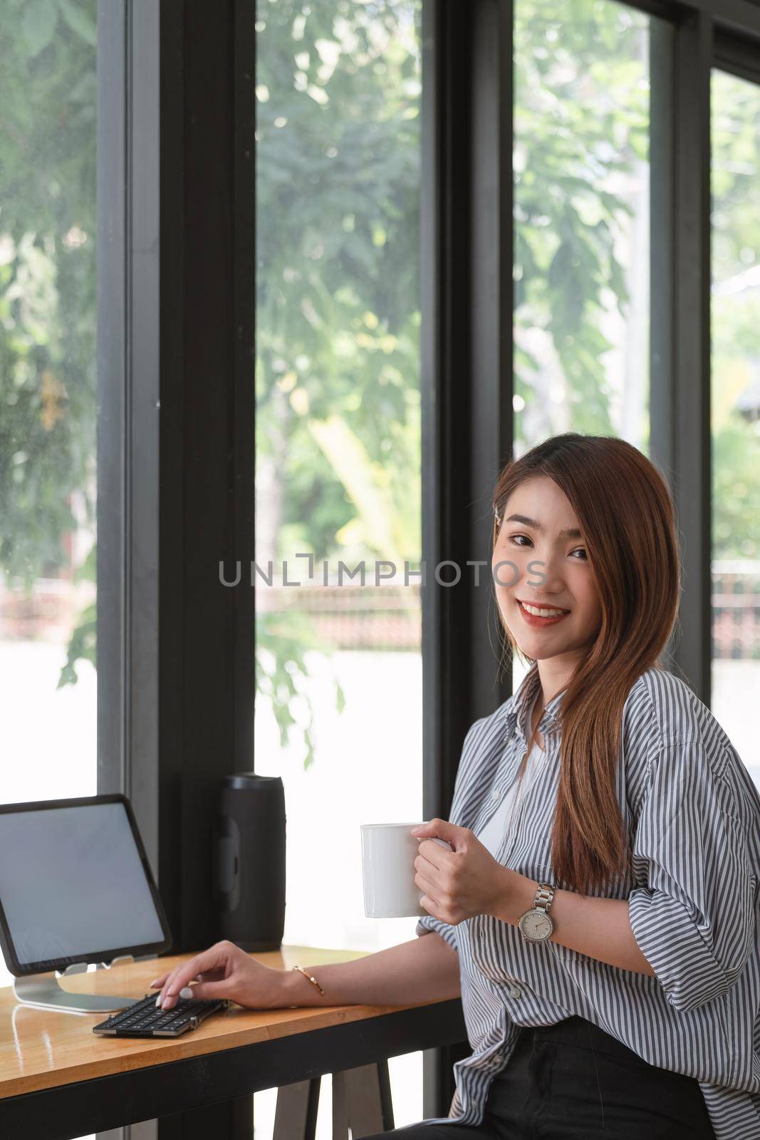 Image of a charming Asian woman working at a coffee shop cafe. Female freelance using digital tablet by nateemee