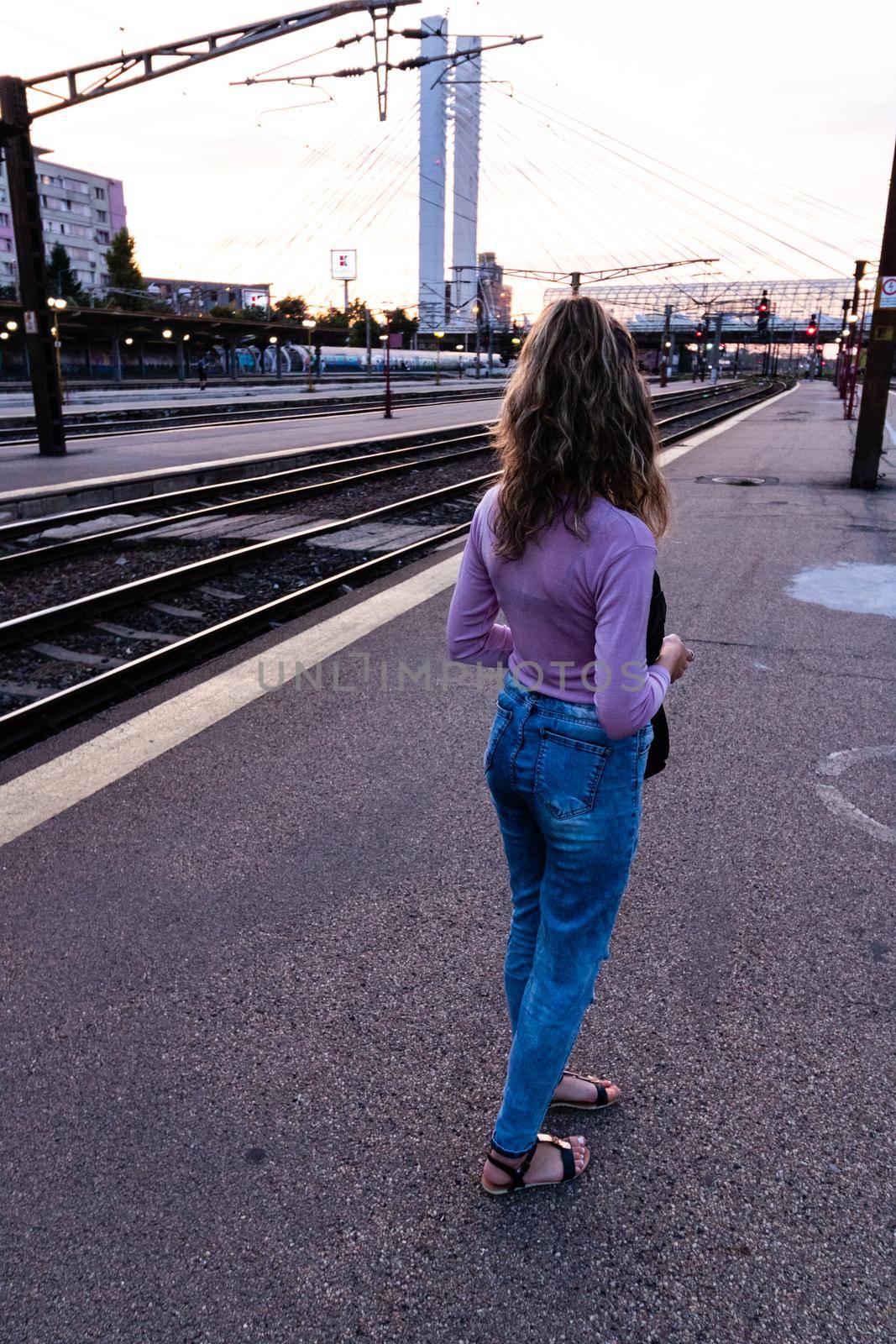 Young girl walking alone on train platform and taking photos on railway station by vladispas