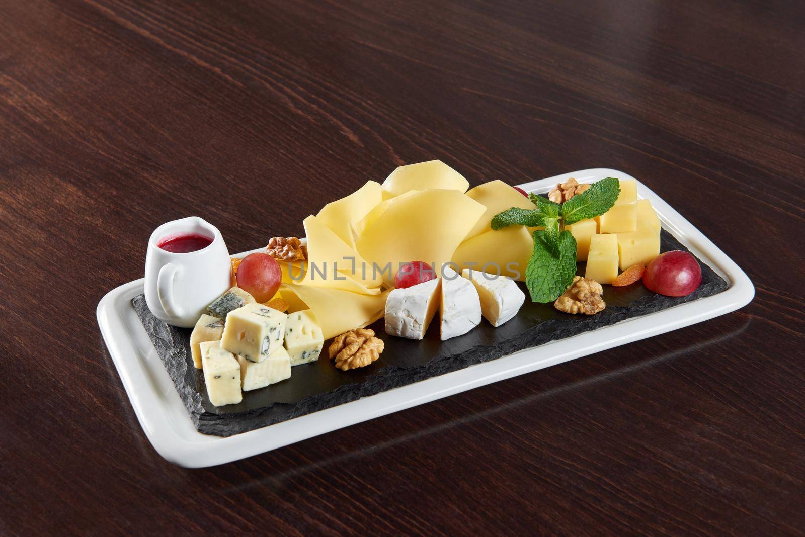 Can you resist this delicious cheese Closeup of delicious various cheese pieces on a wooden plate served with cranberries jam and grapes