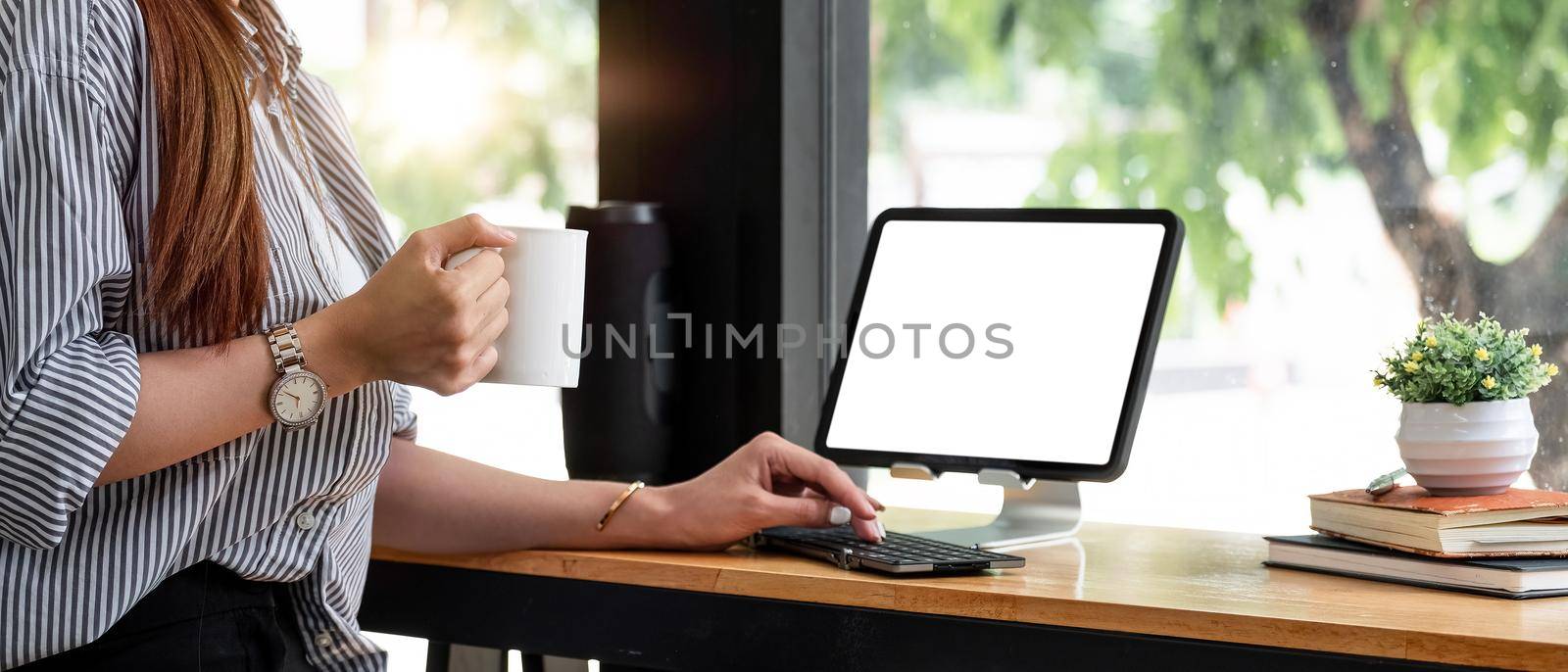 Woman hand holding cup of coffee and using digital tablet. Female working at coffee shop freelance concept by nateemee
