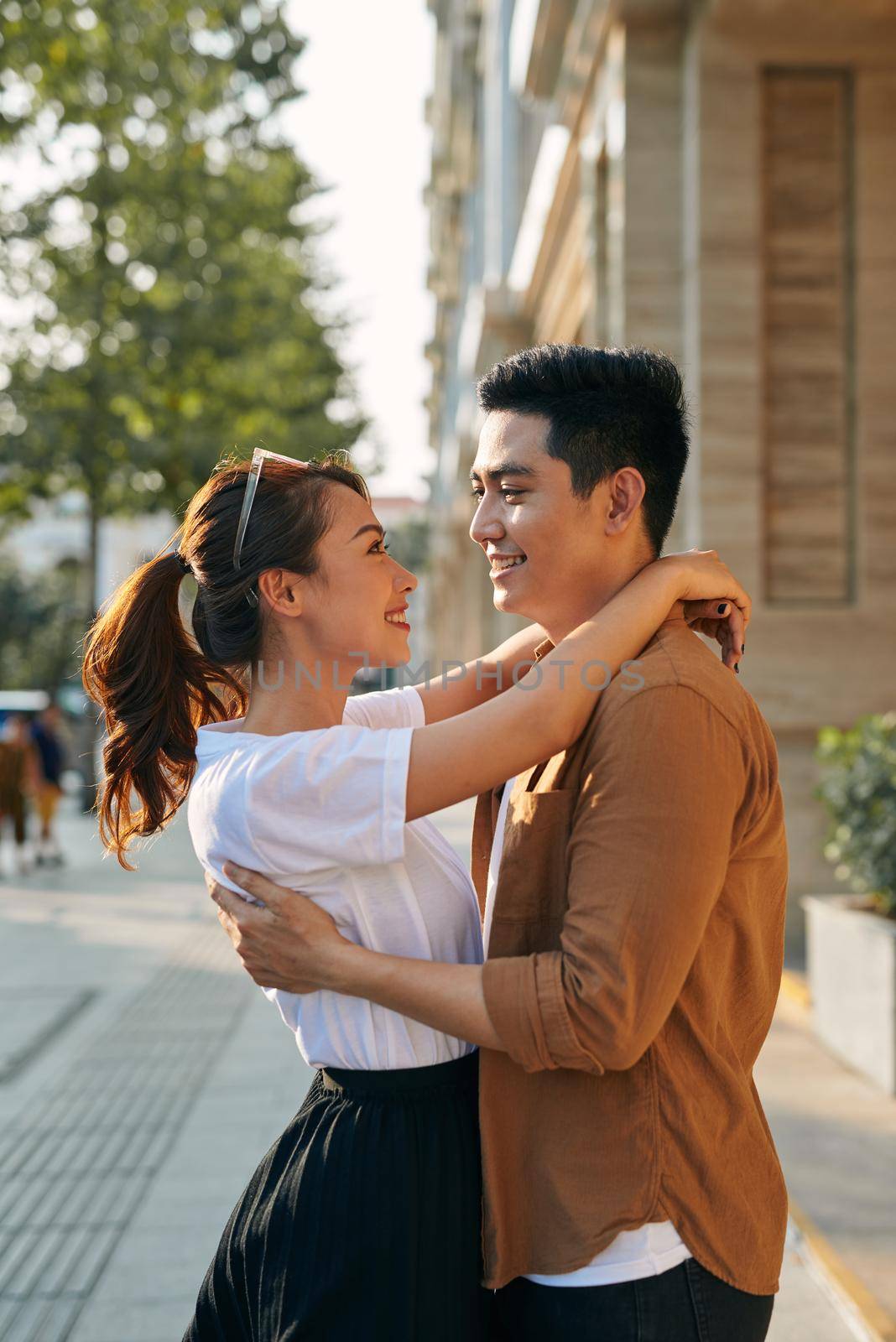 Rear view of a young couple hugging in a destination city while standing in the shopping district near a luxury quality shoe store, outdoors by makidotvn