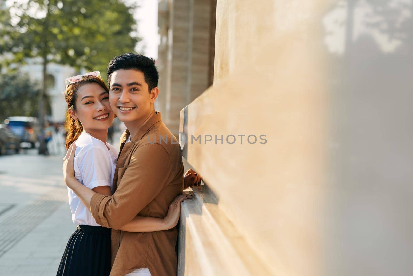 Rear view of a young couple hugging in a destination city while standing in the shopping district near a luxury quality shoe store, outdoors