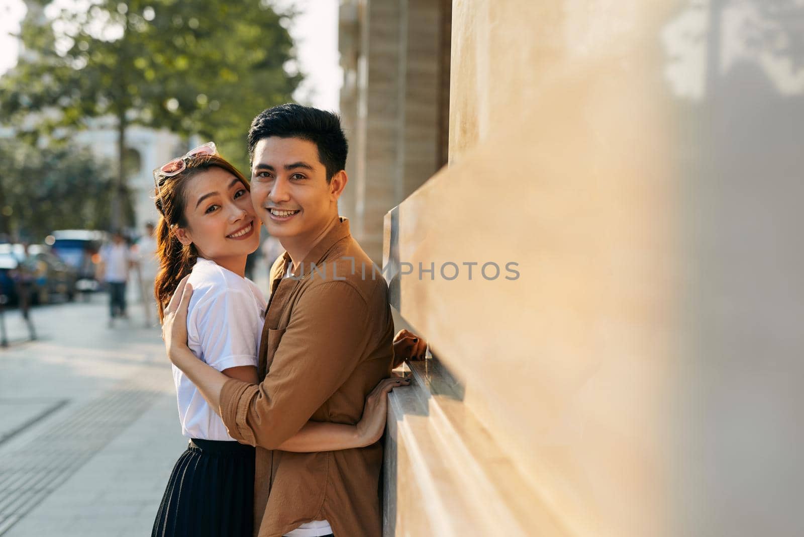 Rear view of a young couple hugging in a destination city while standing in the shopping district near a luxury quality shoe store, outdoors