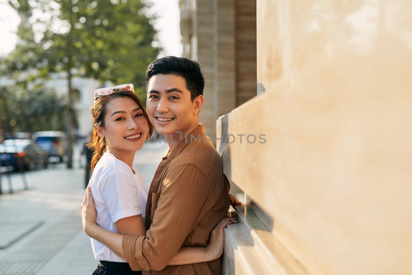 Rear view of a young couple hugging in a destination city while standing in the shopping district near a luxury quality shoe store, outdoors