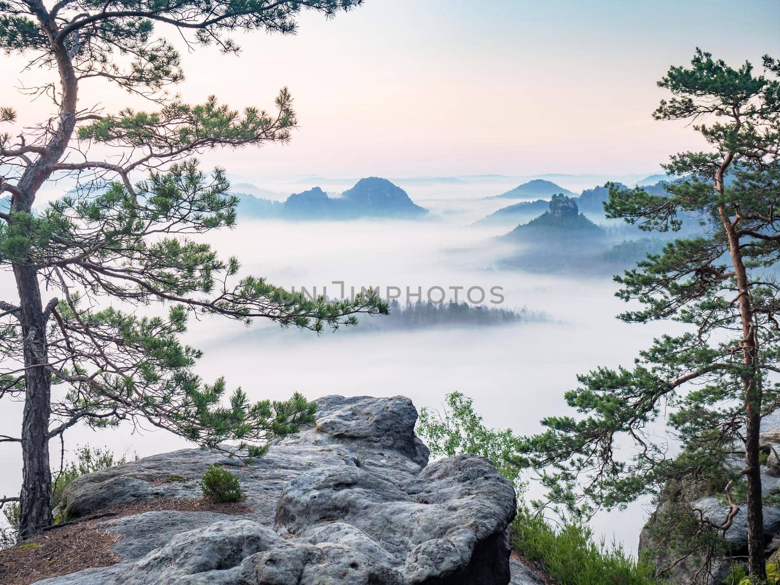 Beautiful morning view Saxony Switzerland. Sandstone peaks and hills increased from foggy background, the misty horizon  is orange due to the first sun rays.