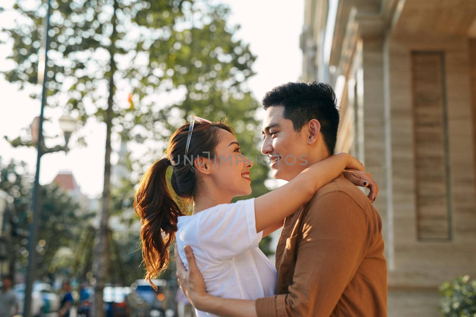 Rear view of a young couple hugging in a destination city while standing in the shopping district near a luxury quality shoe store, outdoors