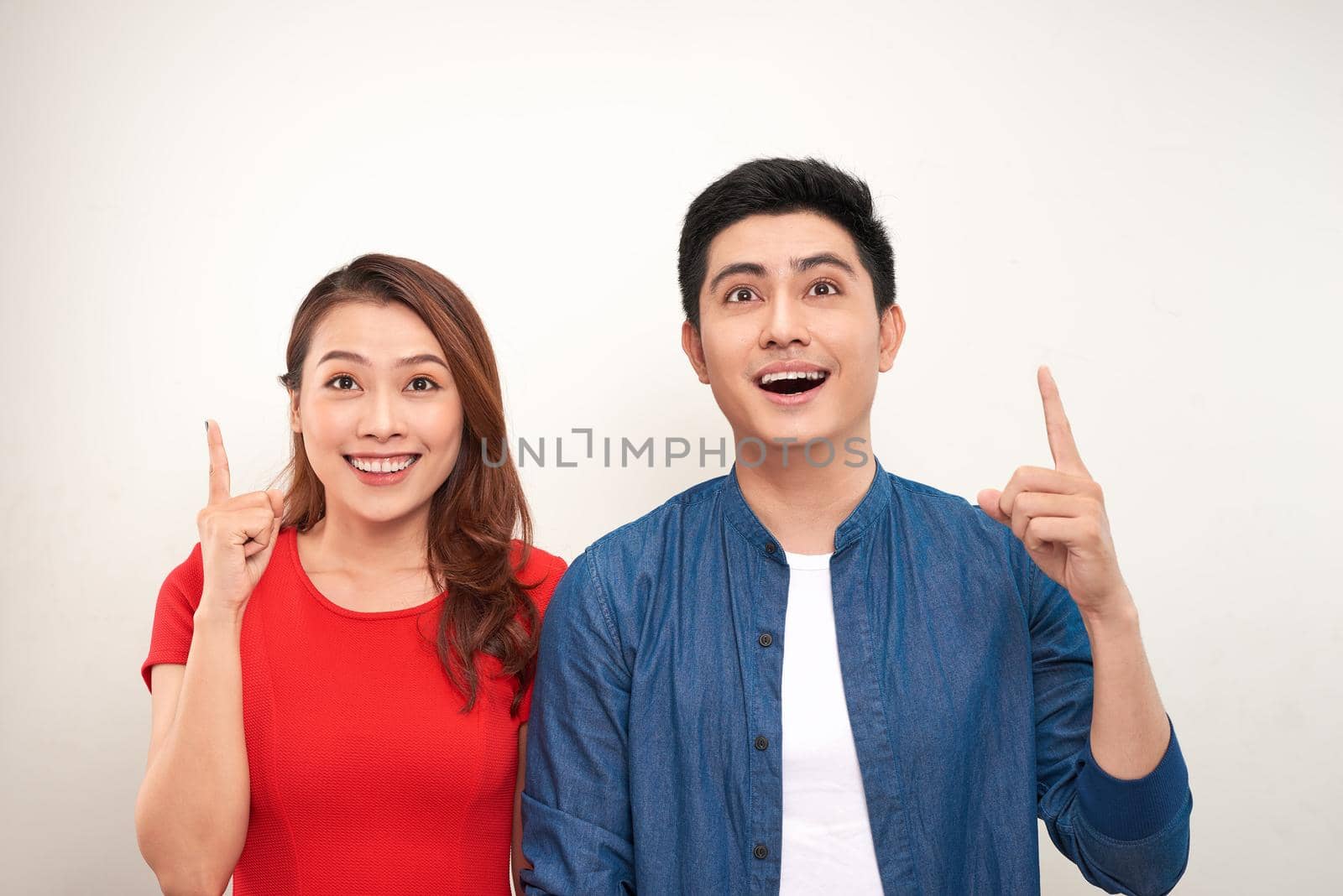 Cheerful asian couple standing isolated over white background, pointing fingers 