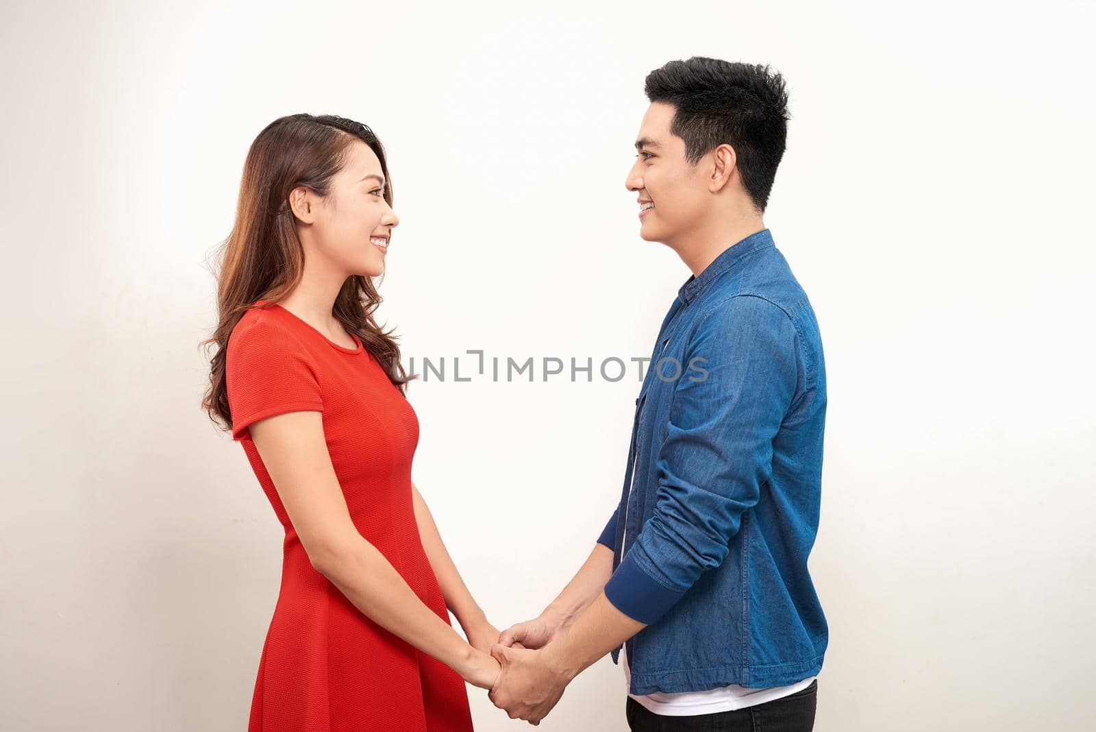 Happy young couple holding hands and laughing on white background