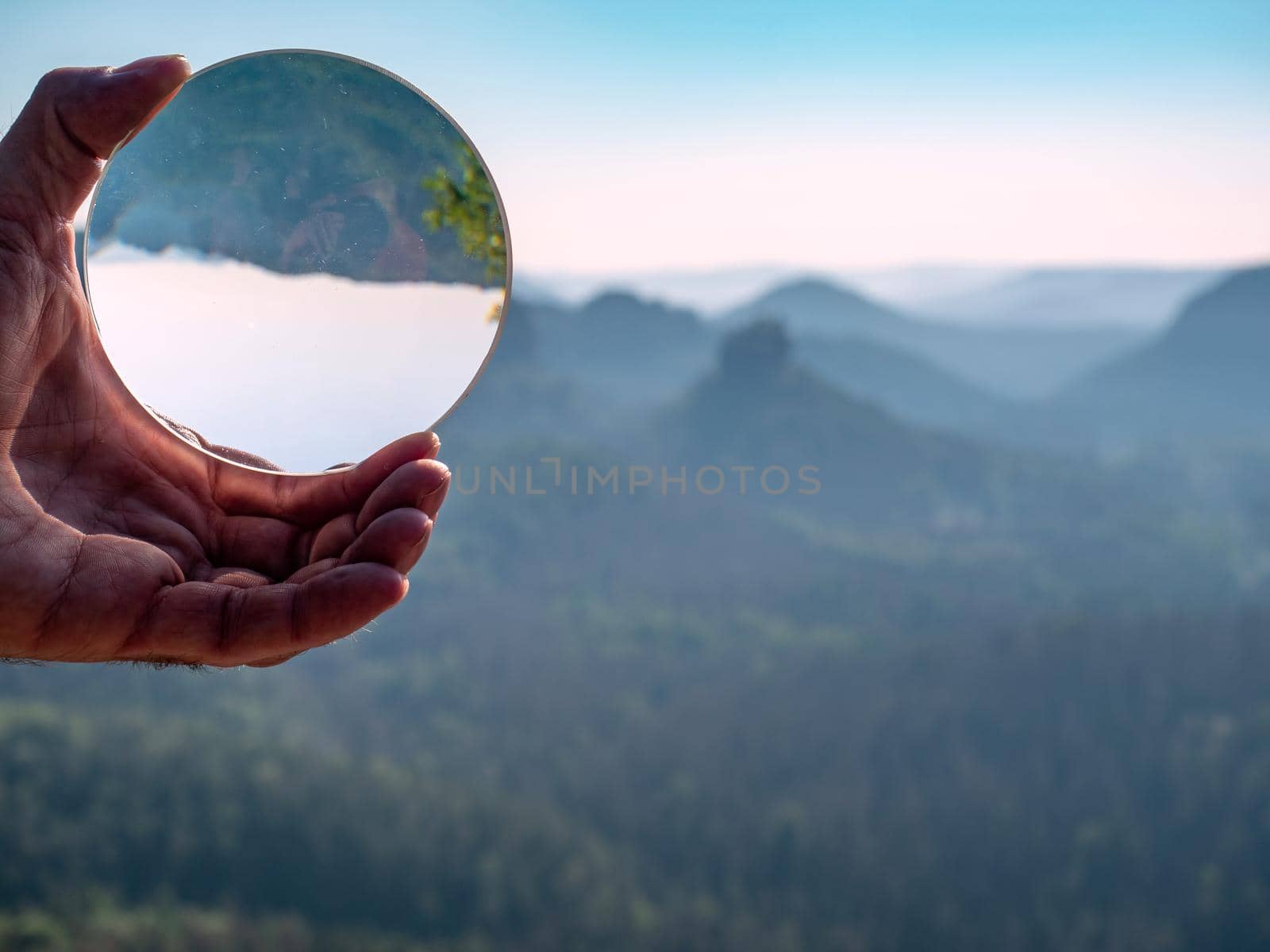 Sunset over valley with sharp hills captured in glass ball, reflection of wavy horizon and  trees silhouettes.