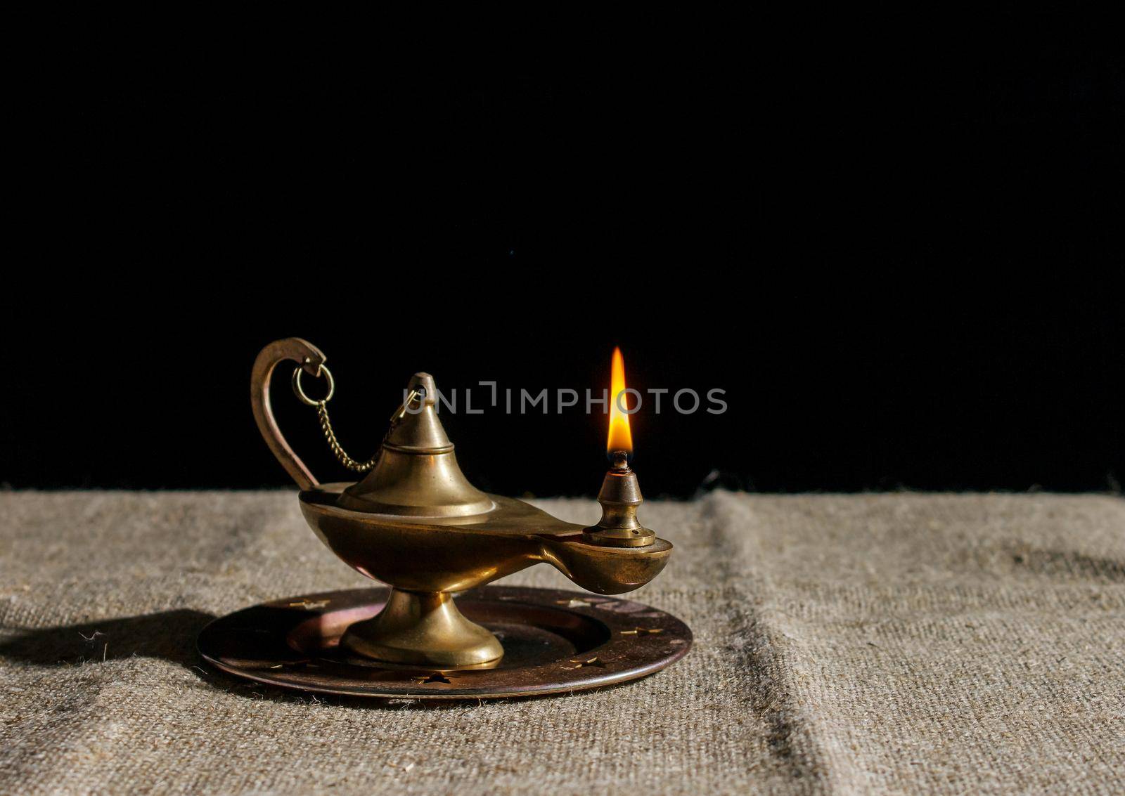 burning magic lamp of aladdin on table. indoor closeup on black background