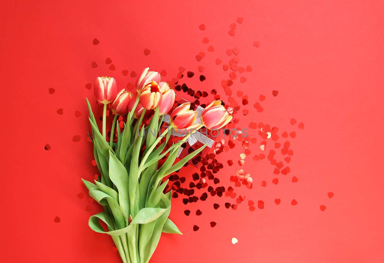 Spring beautiful tulip flowers on bright red background with heart tinsel. by nightlyviolet