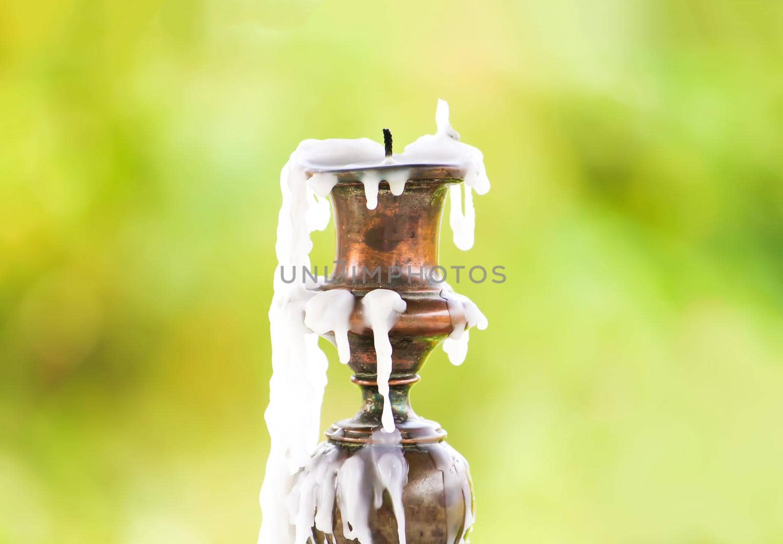 Vintage table candlestick with candle wax on blurred nature background.