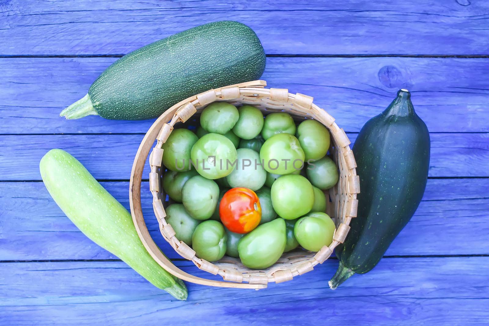 Zucchini and unripe tomatoes on wooden boards outdoors by nightlyviolet