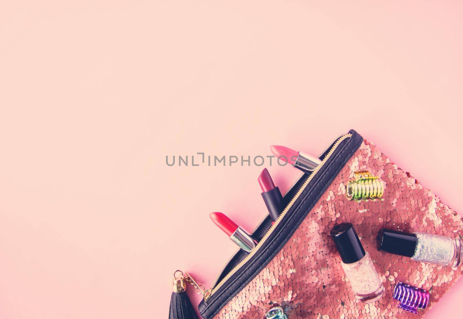 Bright composition of fashion accessories. Glitter sequins cosmetic bag with lipsticks and nail polishes. Object on soft pastel background. Flat lay, top view.